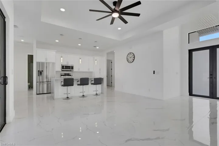Unfurnished living room with a tray ceiling, french doors, a ceiling fan, recessed lighting, and light marble finish floors