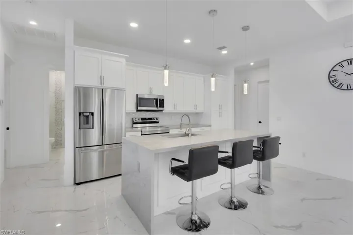 Kitchen featuring stainless steel appliances, light stone countertops, pendant lighting, a kitchen breakfast bar, and white cabinetry
