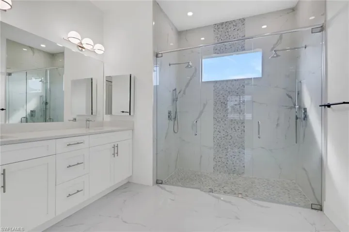 Full bath with double vanity, a marble finish shower, recessed lighting, and light marble finish floors