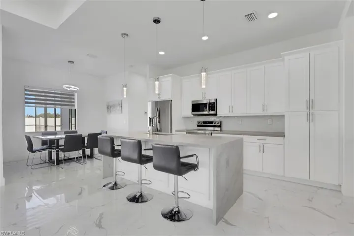 Kitchen featuring decorative light fixtures, an island with sink, a kitchen bar, and white cabinets