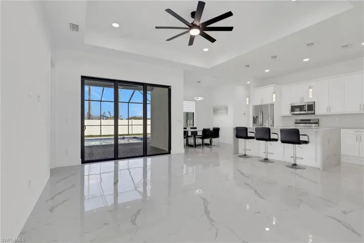 Living room featuring ceiling fan, a tray ceiling, light marble finish flooring, and recessed lighting