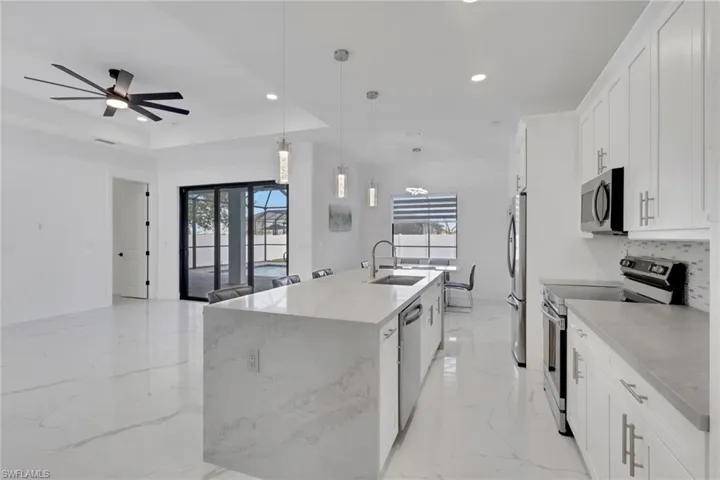 Kitchen with stainless steel appliances, decorative light fixtures, healthy amount of natural light, white cabinets, and a tray ceiling