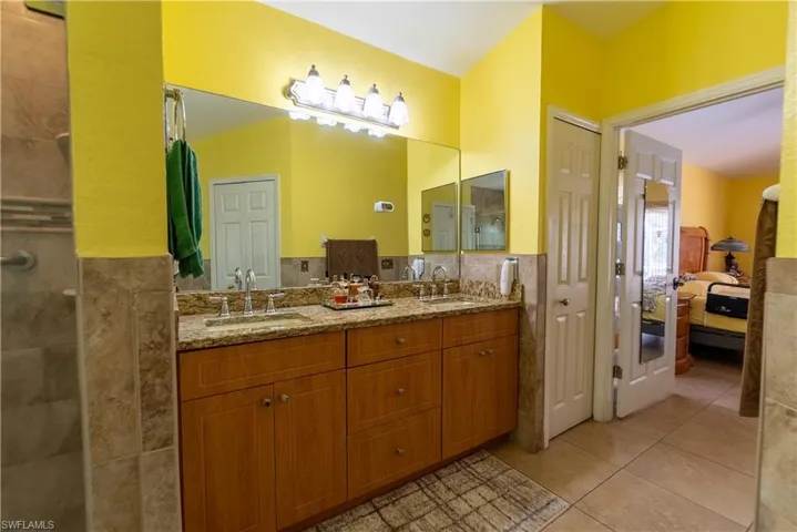 Ensuite bathroom with tile walls, a tile shower, a sink, and tile patterned floors