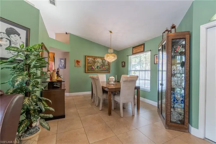 Dining room with a chandelier, lofted ceiling, light tile patterned floors, baseboards, and visible vents