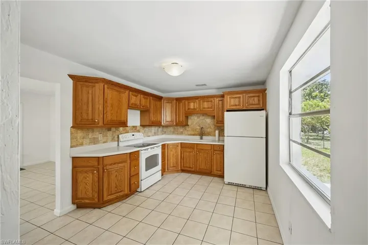 Kitchen with white appliances, light tile patterned floors, tasteful backsplash, and a sink