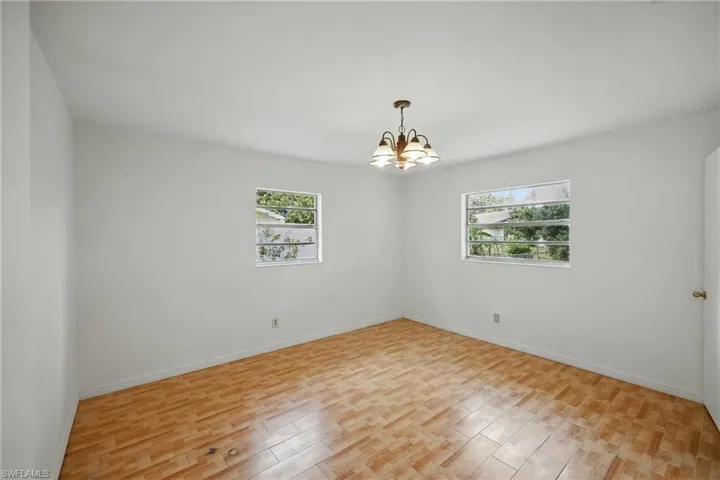 Spare room featuring a chandelier, light wood-type flooring, and baseboards
