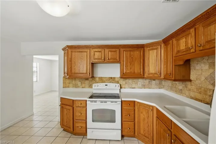 Kitchen featuring white electric range, backsplash, light tile patterned flooring, and light countertops