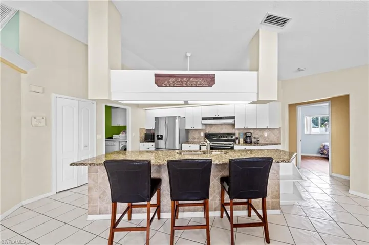 Kitchen featuring stainless steel appliances, under cabinet range hood, washer and clothes dryer, a sink, and backsplash