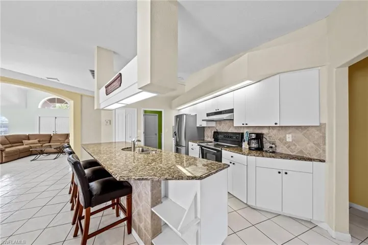 Kitchen with range with electric cooktop, under cabinet range hood, a sink, stainless steel refrigerator with ice dispenser, and tasteful backsplash