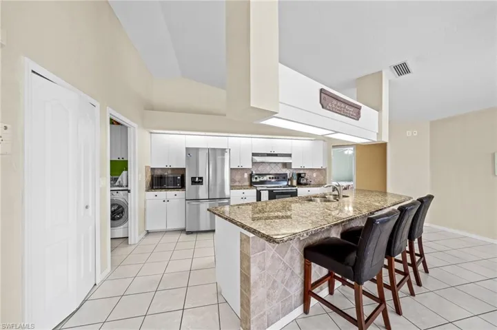 Kitchen featuring appliances with stainless steel finishes, under cabinet range hood, washer / clothes dryer, light tile patterned floors, and vaulted ceiling