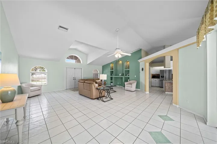 Living area with vaulted ceiling, a ceiling fan, light tile patterned floors, arched walkways, and baseboards