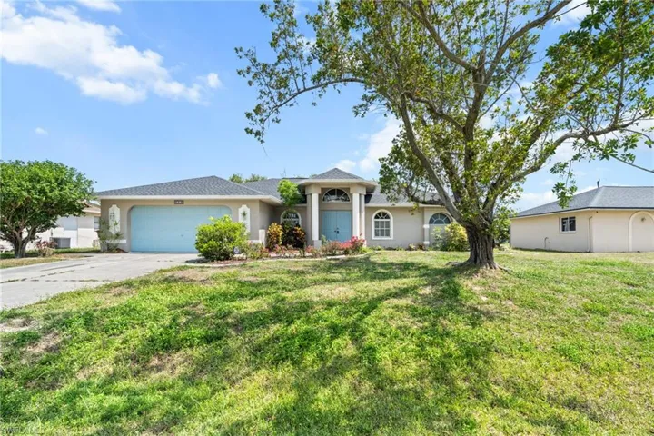 View of front of property featuring a garage, driveway, a front yard, and stucco siding