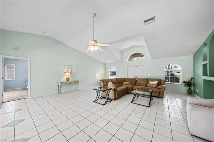 Living area with lofted ceiling, light tile patterned floors, and ceiling fan