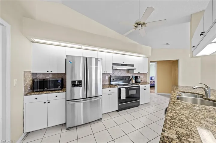 Kitchen with stainless steel appliances, under cabinet range hood, a sink, lofted ceiling, and tasteful backsplash