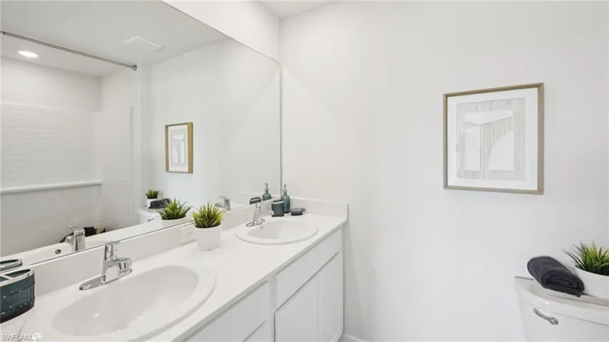 Model Home. Bathroom featuring a large vanity with dual sinks and chrome faucets, a full-width mirror, and white subway tile in the shower area