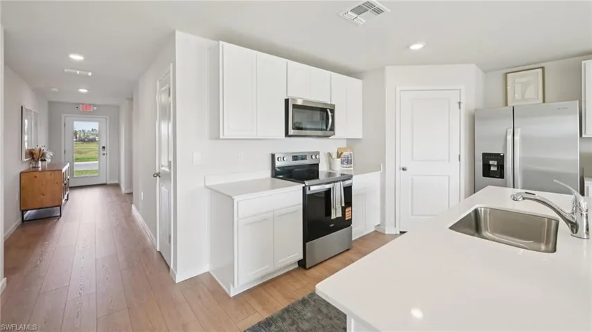 Model Home. The kitchen features white cabinetry, stainless steel appliances, and a central island with an integrated sink and faucet