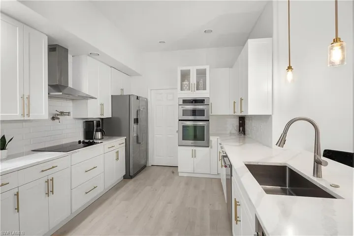 Contemporary kitchen featuring white cabinetry, light-toned wood-finish flooring, stainless steel appliances, a pot filler, and pendant lighting
