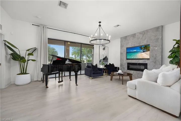 Spacious interior featuring light wood-finish flooring, a contemporary chandelier, and a floor-to-ceiling accent wall with a built-in electric fireplace