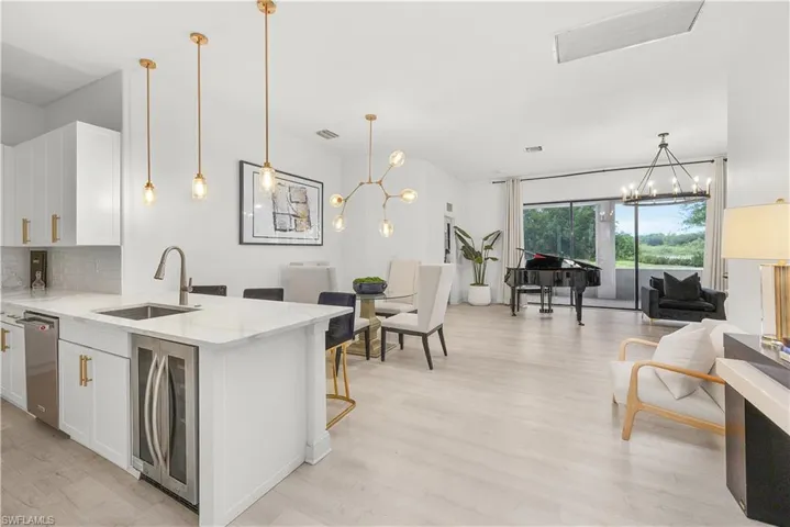 Open-concept living space featuring light wood-finish flooring and a kitchen island with a built-in beverage cooler and stainless steel sink