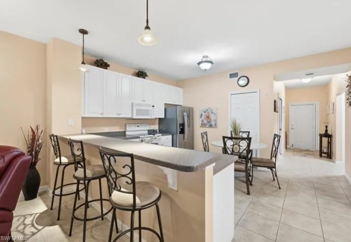 Kitchen with dark countertops, a kitchen breakfast bar, a peninsula, stainless steel fridge, and white cabinetry
