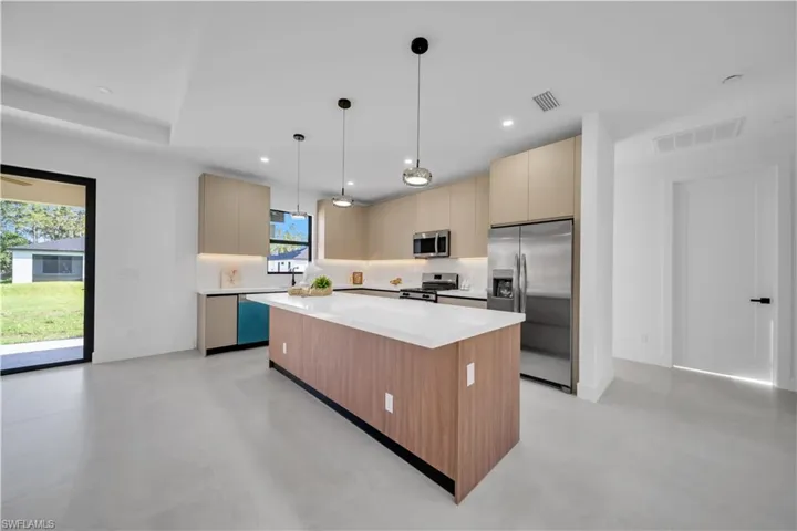 Modern kitchen featuring a large central island with a white countertop, two-tone cabinetry, stainless steel appliances, and sleek pendant lighting