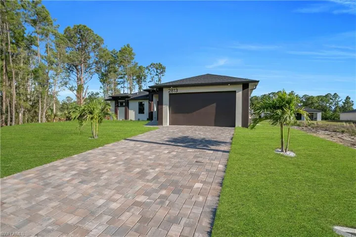 Contemporary exterior featuring a paver driveway, an attached garage, a dark garage door, and a manicured lawn