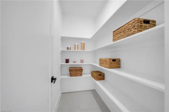 Walk-in pantry featuring expansive shelving, white painted walls, and a light-colored flooring material