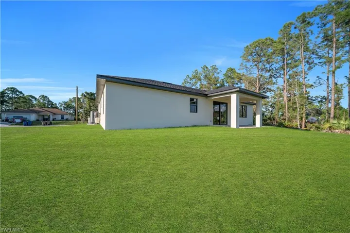 Expansive green lawn with a newly constructed residence featuring a covered patio and contemporary exterior finish