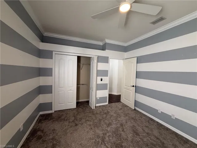Unfurnished bedroom with wallpapered walls, dark colored carpet, ornamental molding, a ceiling fan, and a closet