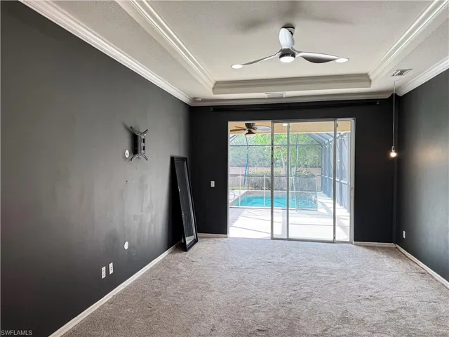 Carpeted empty room with ceiling fan, a sunroom, crown molding, and a tray ceiling