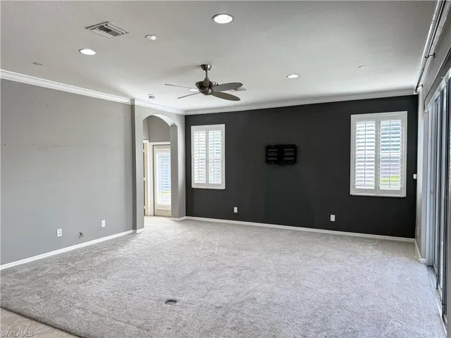 Spare room with a ceiling fan, crown molding, arched walkways, light carpet, and plenty of natural light
