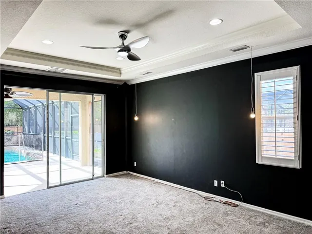 Carpeted spare room featuring ceiling fan, ornamental molding, a tray ceiling, a sunroom, and a textured ceiling