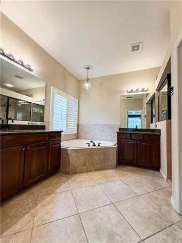 Full bathroom featuring two vanities, a bath, hanging lights, and light tile patterned floors