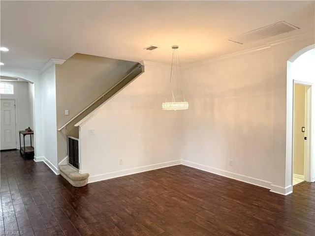 Unfurnished living room featuring arched walkways, crown molding, and dark wood-style floors