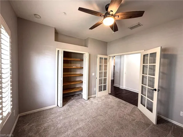 Unfurnished bedroom with french doors, ceiling fan, dark carpet, and a closet