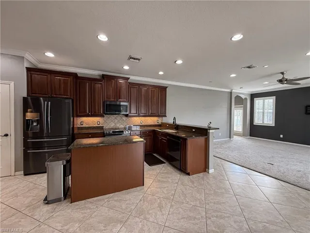 Kitchen featuring arched walkways, black appliances, ornamental molding, a center island, and dark stone countertops