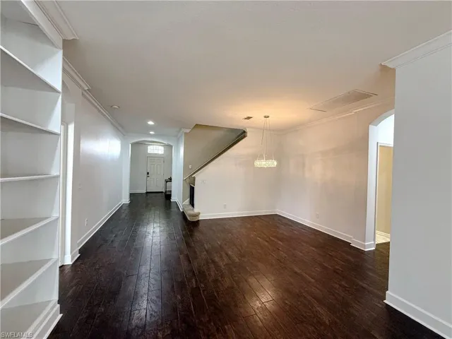 Unfurnished living room featuring arched walkways, dark wood-type flooring, crown molding, and recessed lighting