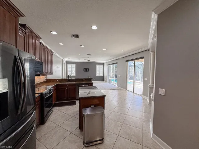 Kitchen featuring ornamental molding, black appliances, open floor plan, dark wood finish cabinets, and a peninsula