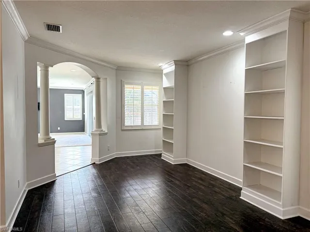 Unfurnished room with arched walkways, ornate columns, ornamental molding, a textured ceiling, and dark wood-style flooring