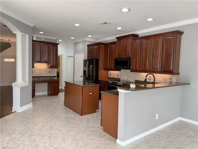 Kitchen featuring arched walkways, a peninsula, dark stone counters, a kitchen island, and black appliances