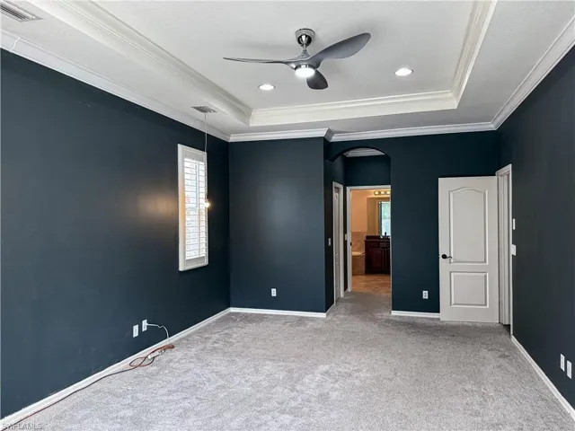 Unfurnished bedroom featuring arched walkways, connected bathroom, light colored carpet, a ceiling fan, and ornamental molding