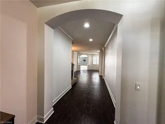 Hall with arched walkways, dark wood-type flooring, recessed lighting, and crown molding