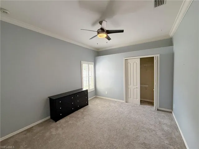Unfurnished bedroom featuring crown molding, light colored carpet, a ceiling fan, and a closet