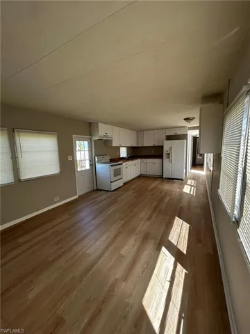 Kitchen with dark countertops, white appliances, white cabinets, dark wood-style flooring, and open floor plan