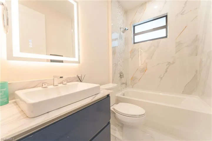 Full bathroom with vanity, tiled shower / bath combo, and toilet