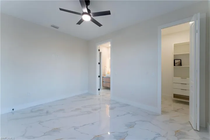 Unfurnished bedroom featuring a walk in closet, ceiling fan, and ensuite bathroom