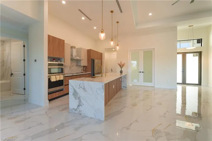 Kitchen with a large island, french doors, hanging light fixtures, and wall chimney range hood
