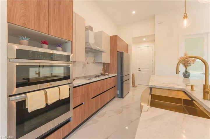 Kitchen featuring light stone countertops, tasteful backsplash, wall chimney exhaust hood, stainless steel appliances, and decorative light fixtures