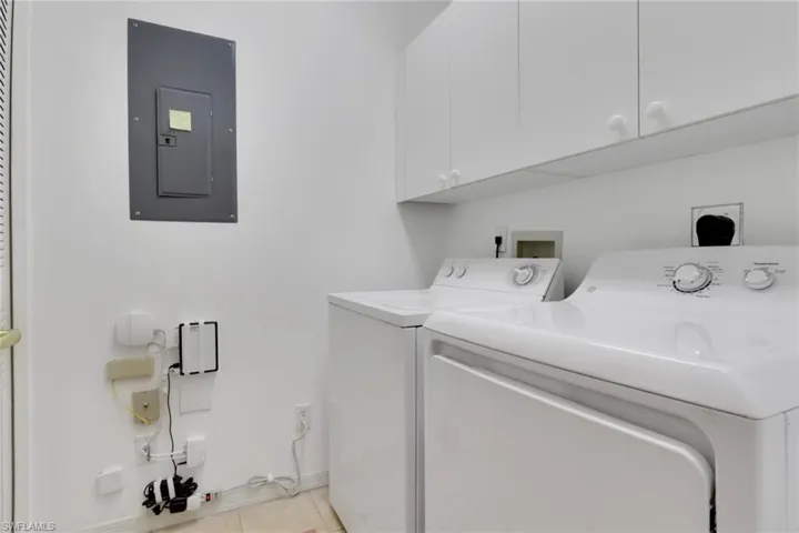 Laundry room featuring electric panel, cabinet space, light tile patterned floors, and independent washer and dryer