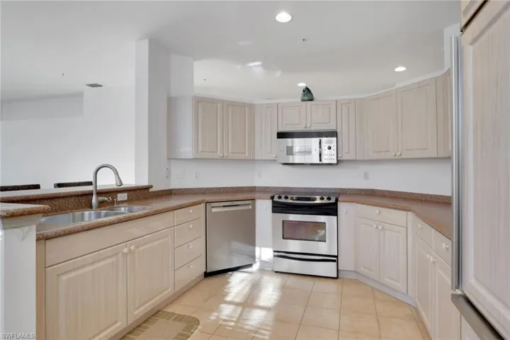 Kitchen with appliances with stainless steel finishes, light tile patterned floors, recessed lighting, and dark stone counters